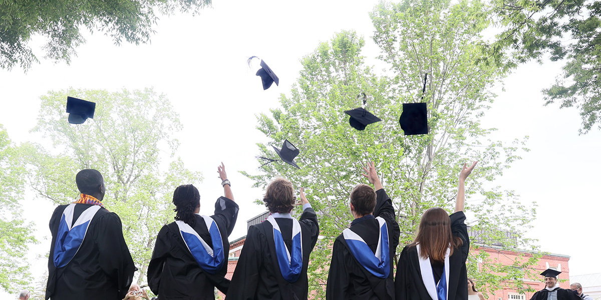 Four students in graduation regalia throwing their mortar boards in the air