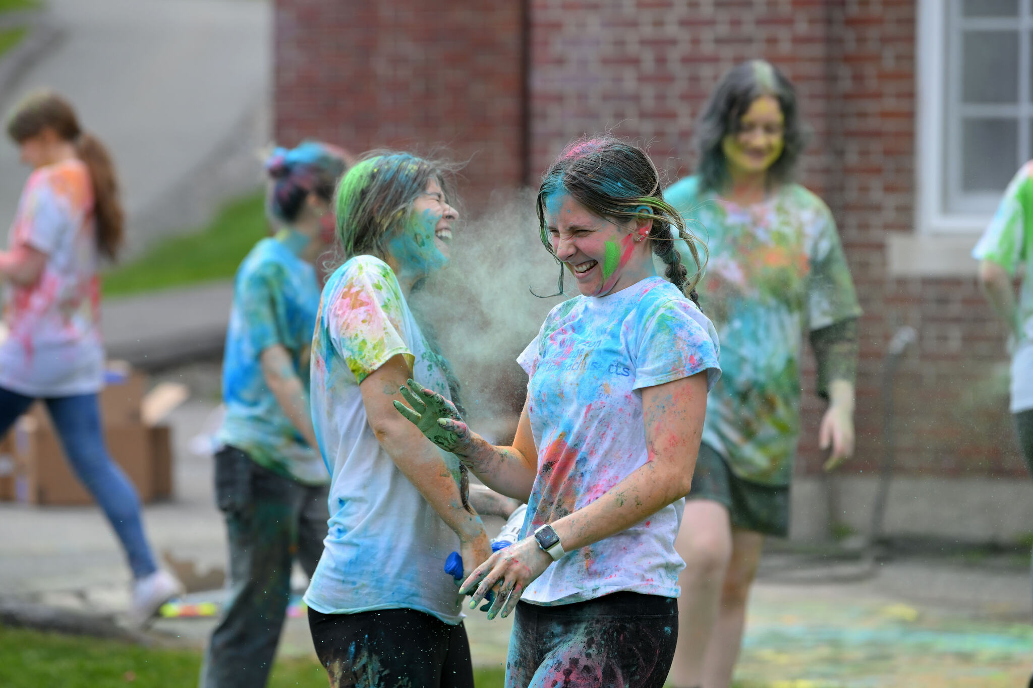 Two students—wearing multicolored t-shirts—laugh together at the college's annual Holi celebration