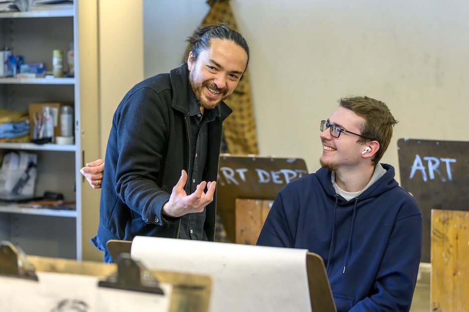 A professor and student smile while in discussion in an art studio