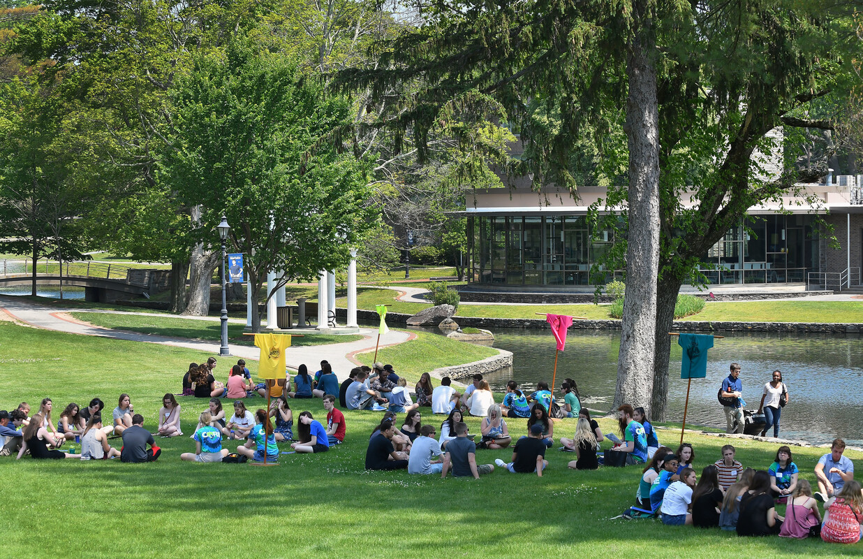 Student sitting on the Chapel lawn by Peacock Pond on a sunny, summer day