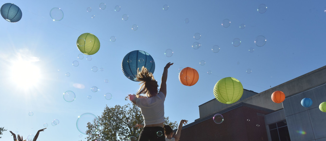 student dancing against a blue sky with a string of paper lanterns diagonally across